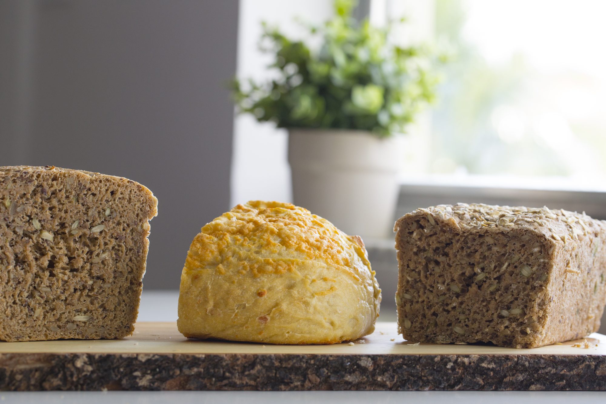 Tre nybakade bröd på en träskiva i morgonljus